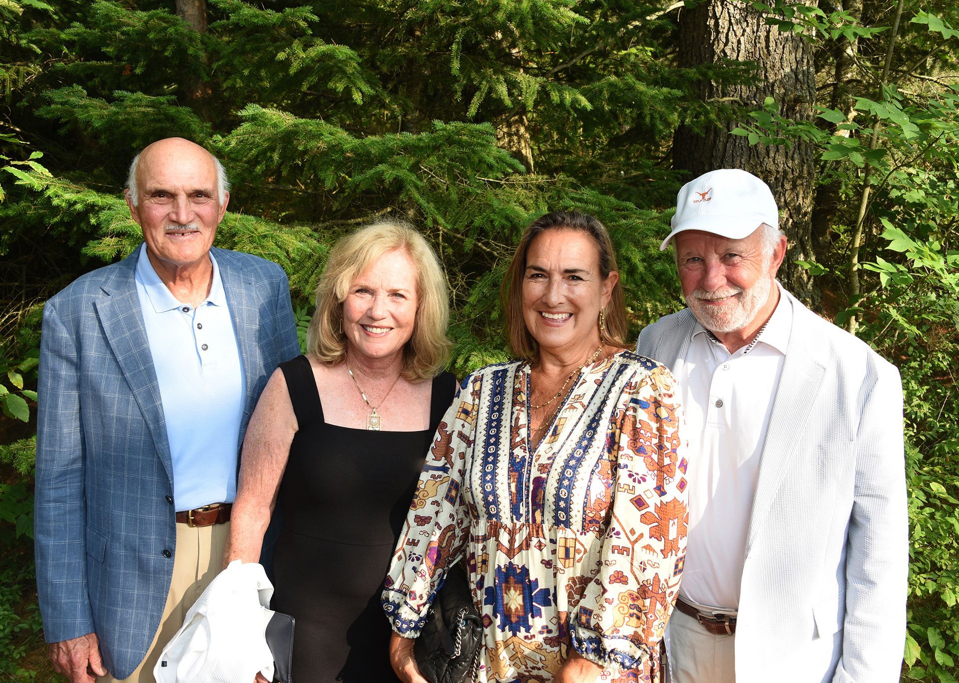 Four people, two men and two women, pose outdoors in front of green foliage.