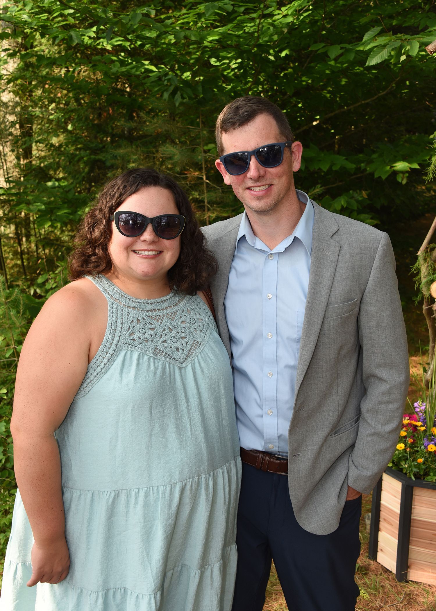 A smiling woman and man wearing sunglasses pose outdoors.