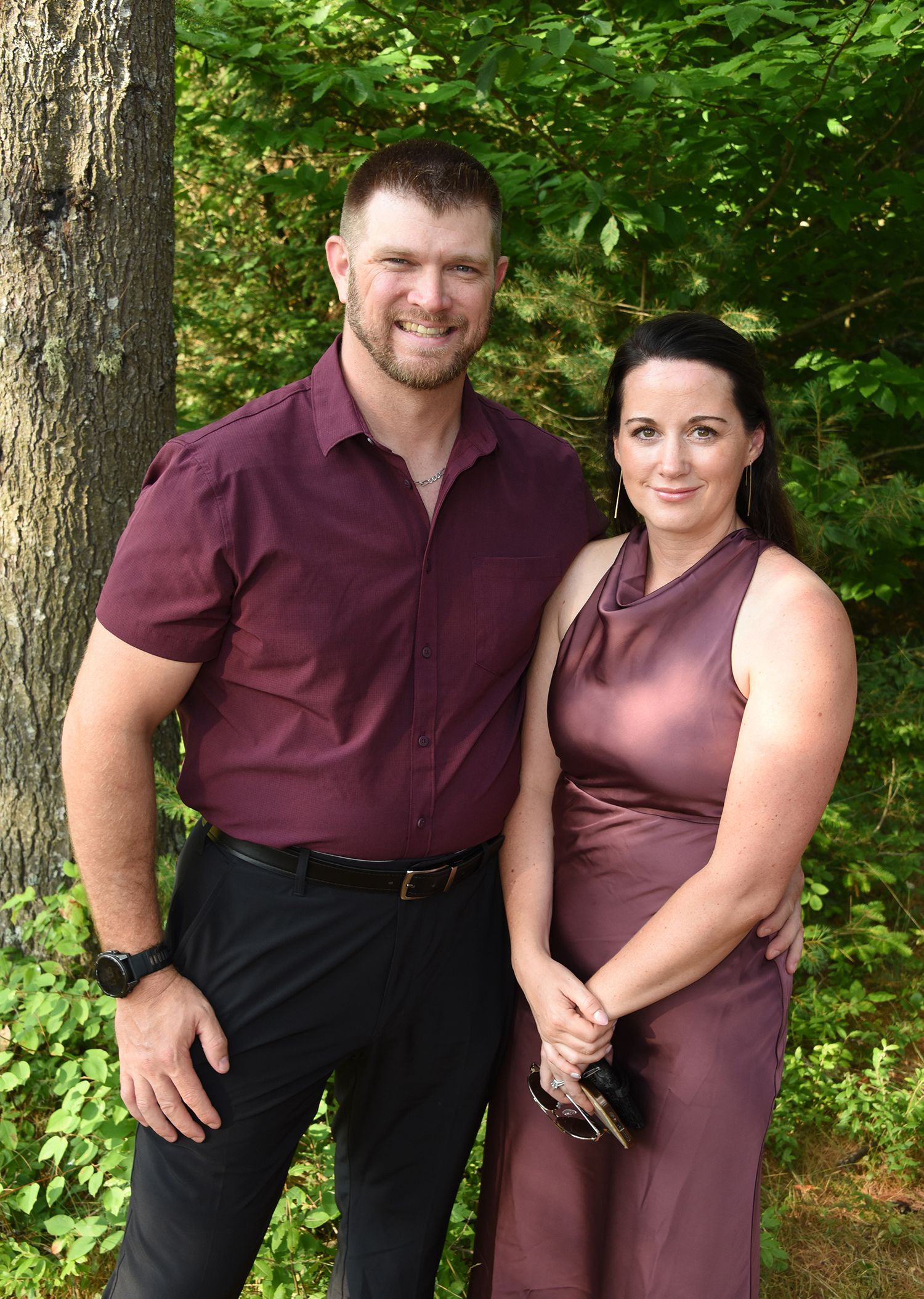 A smiling man and woman in formal attire pose outdoors.