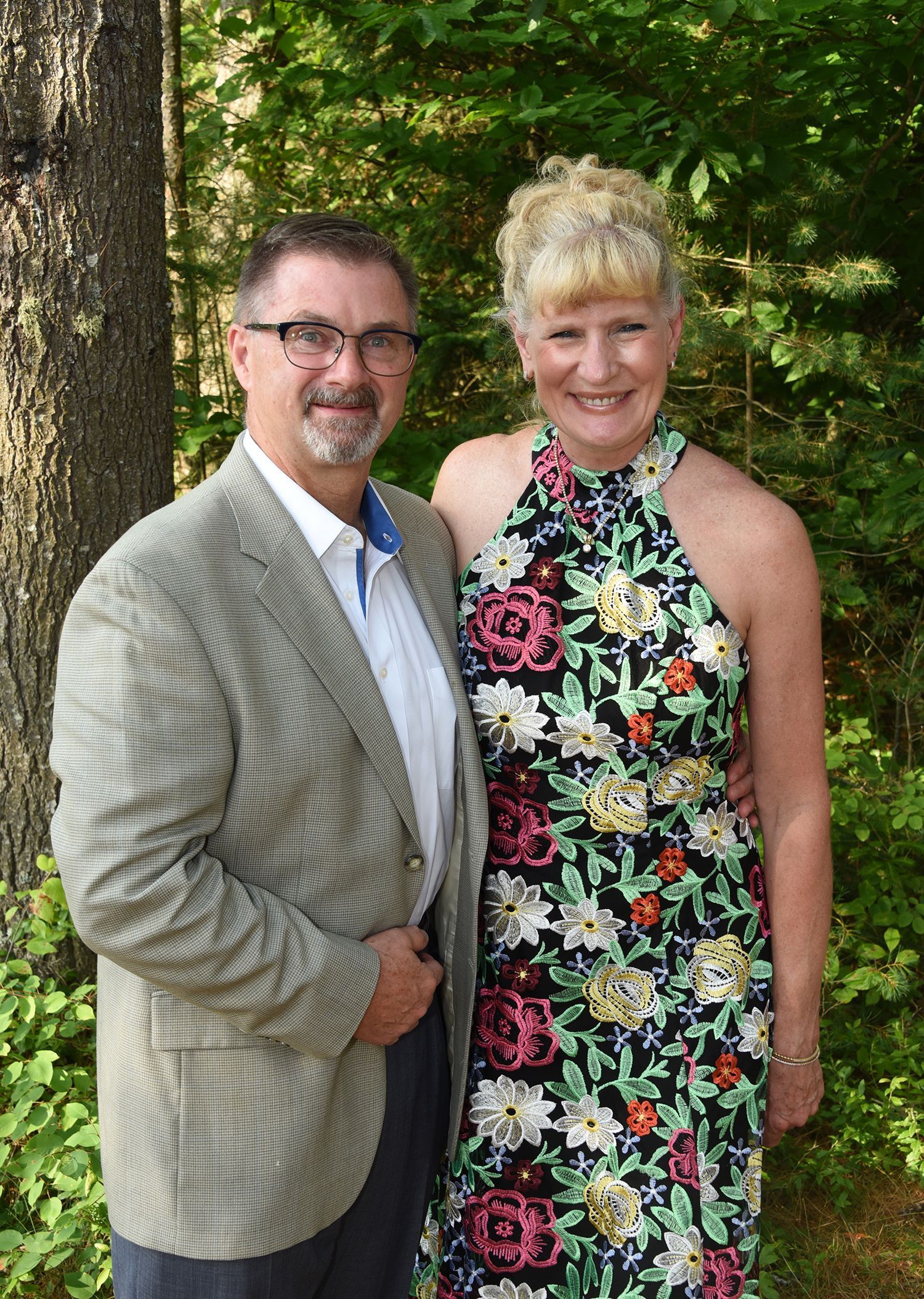 Man and woman standing close together outdoors. The man wears glasses, a jacket, and a white shirt.