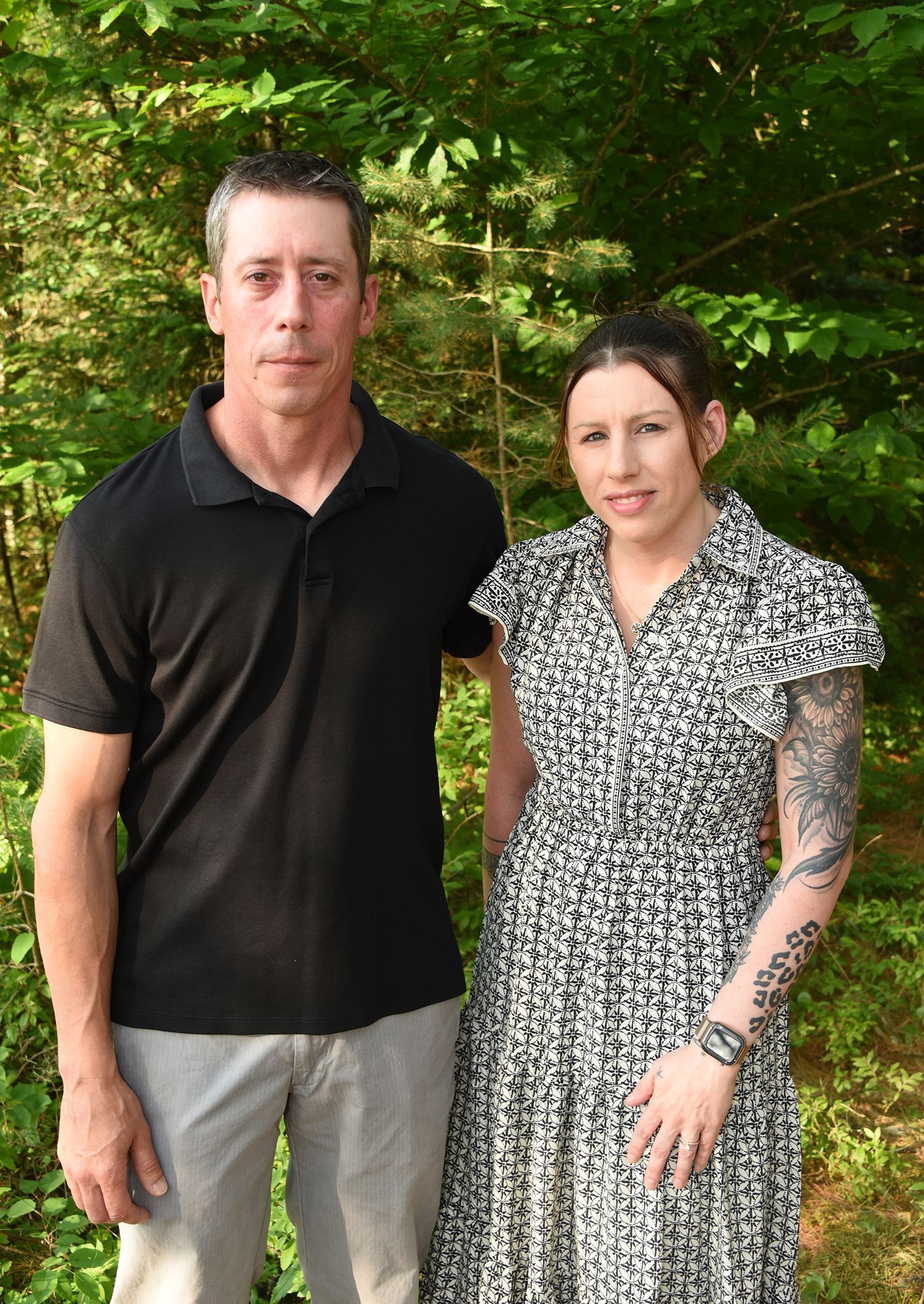 A man and woman standing outdoors. The man wears a black shirt and gray pants.