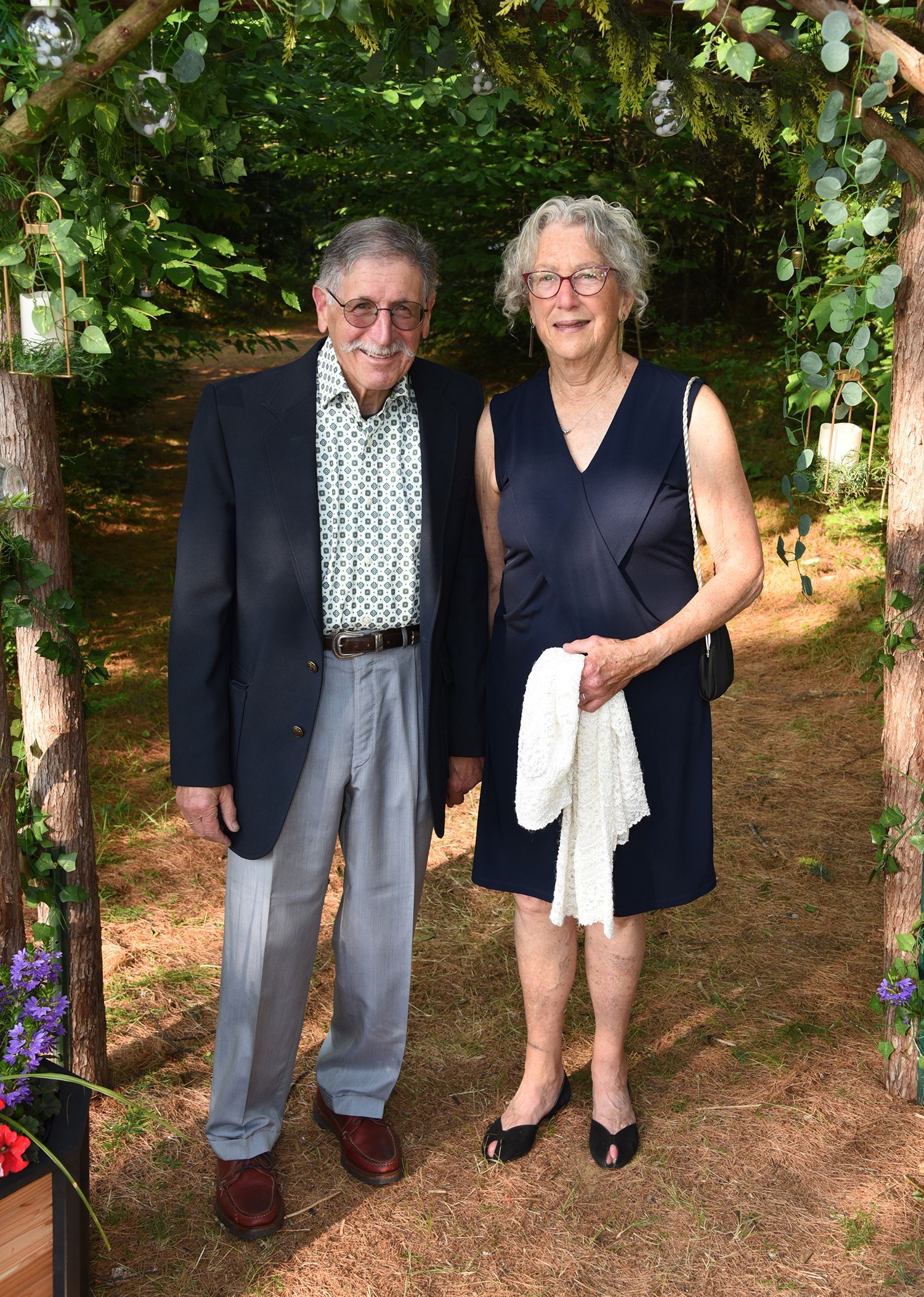 Elderly couple standing under a floral archway, smiling. 