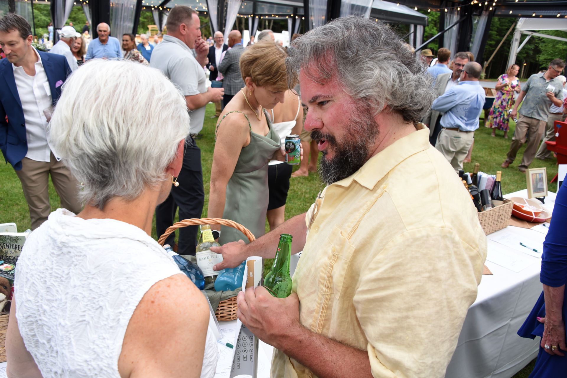 Man with graying hair and beard talking to a woman with short, white hair at an outdoor event.