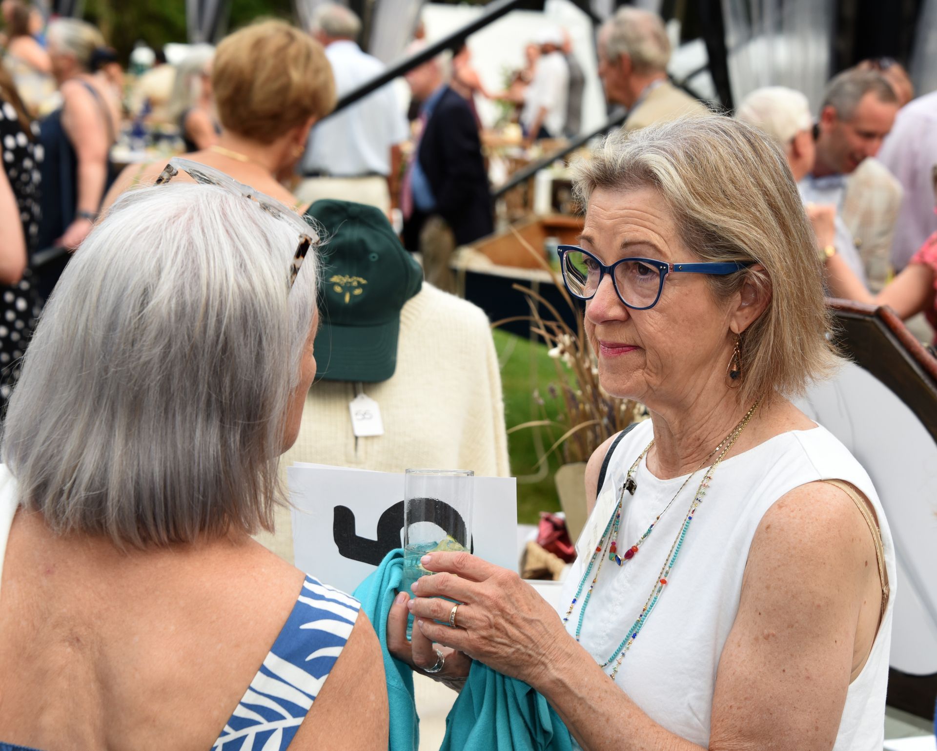 Two older women with gray hair converse at an outdoor market