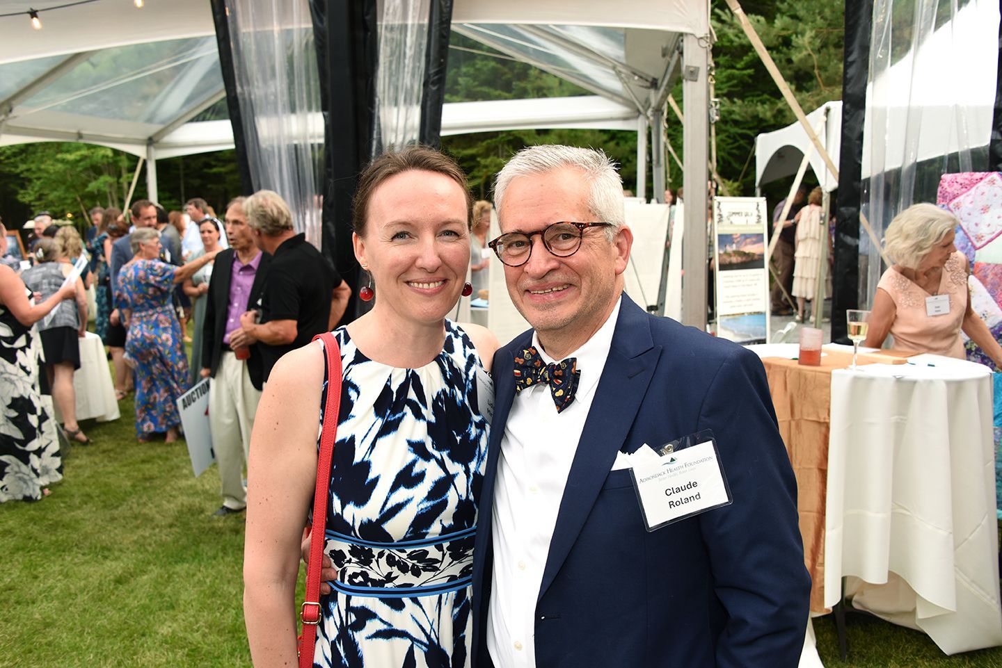 Woman and man smile for the camera at an outdoor event. The woman wears a patterned dress.