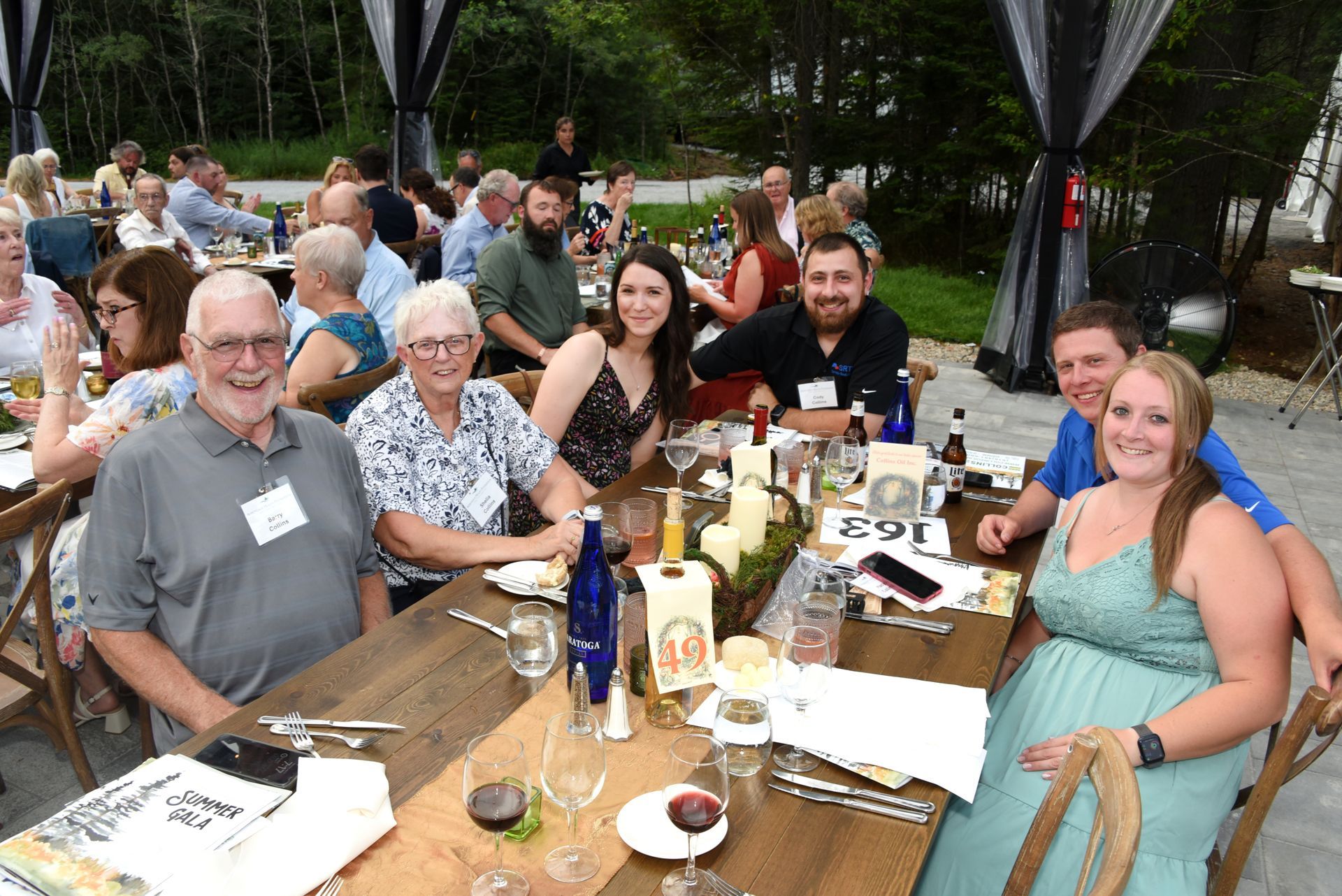 People gathered at long wooden tables outdoors, smiling and dining.