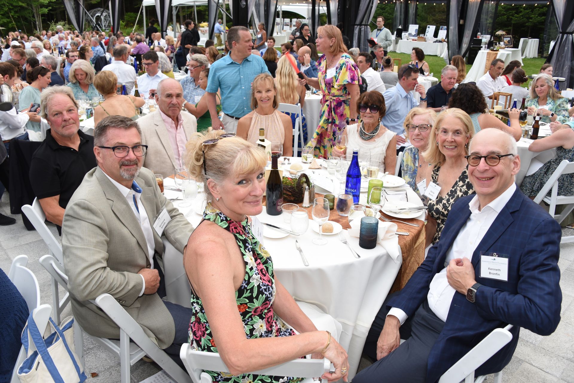 Group of people seated at a round table, attending an outdoor event.