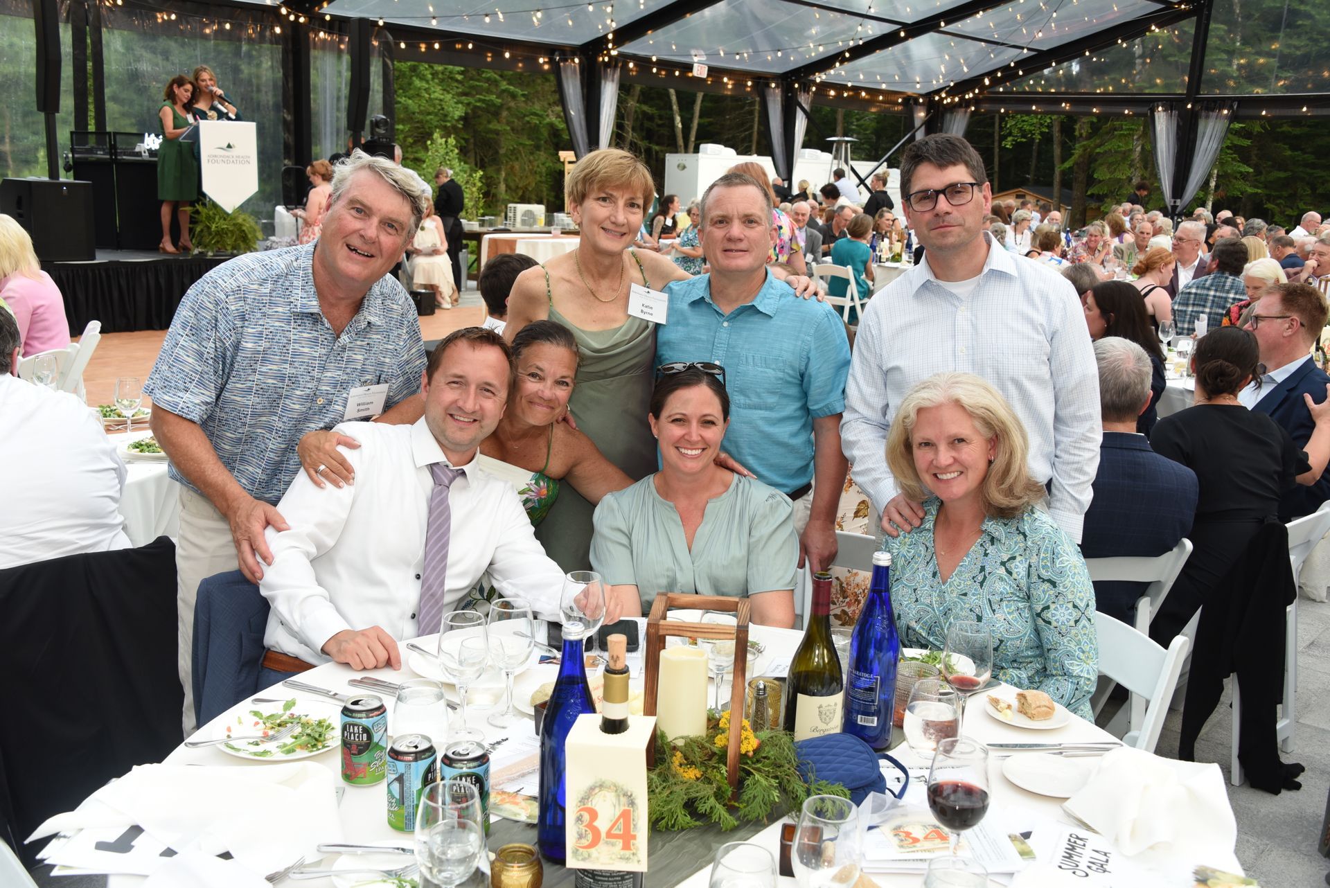 Group photo at outdoor event: smiling people gathered around a table set.