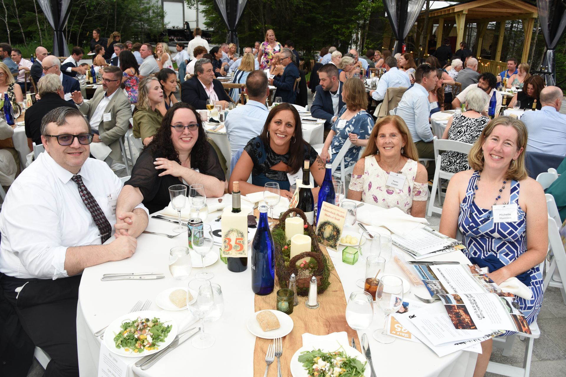 Group of six people seated at a round table outdoors, smiling at the camera.