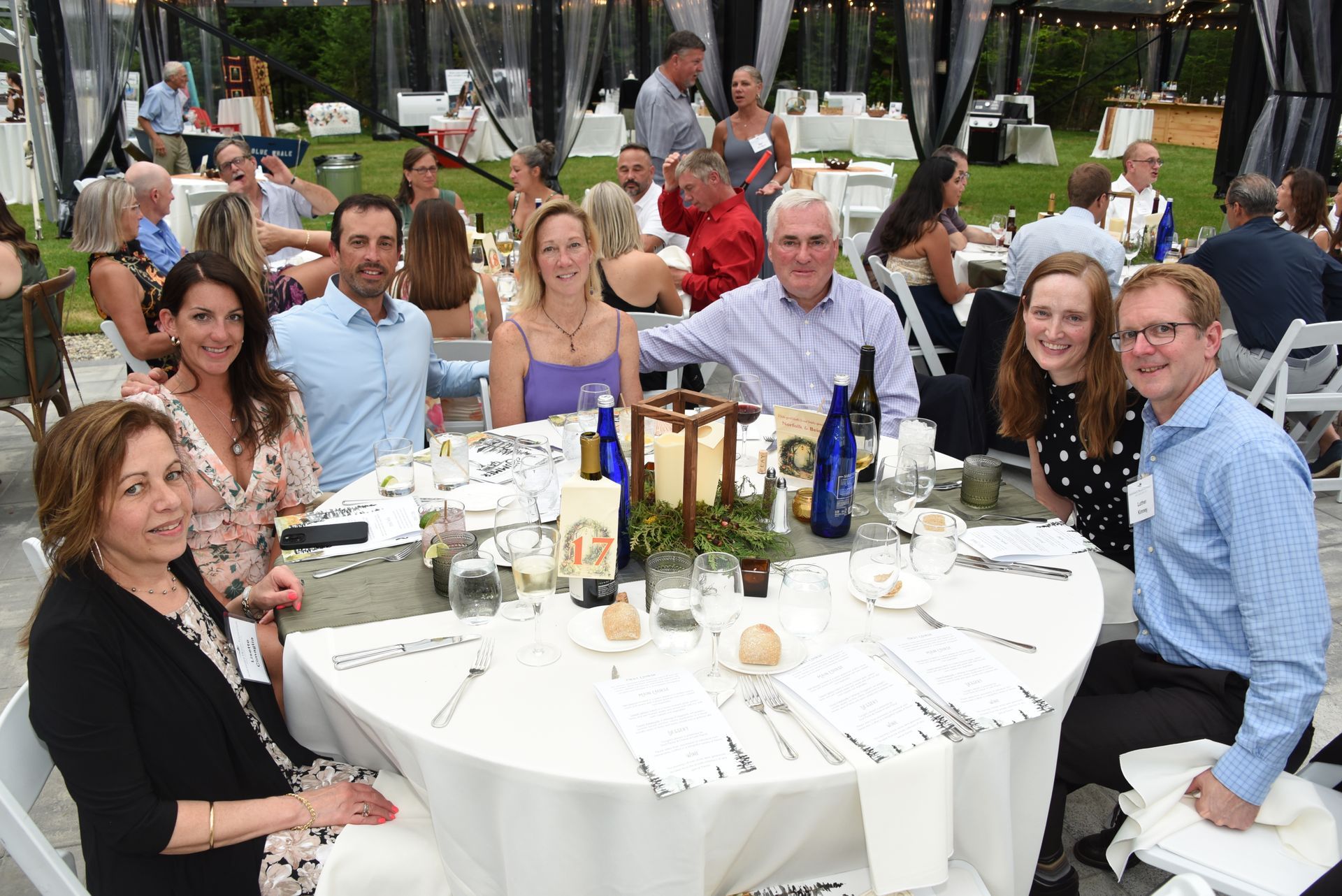 Group of people seated around a round table at an outdoor event. Some smile while others look at the camera.