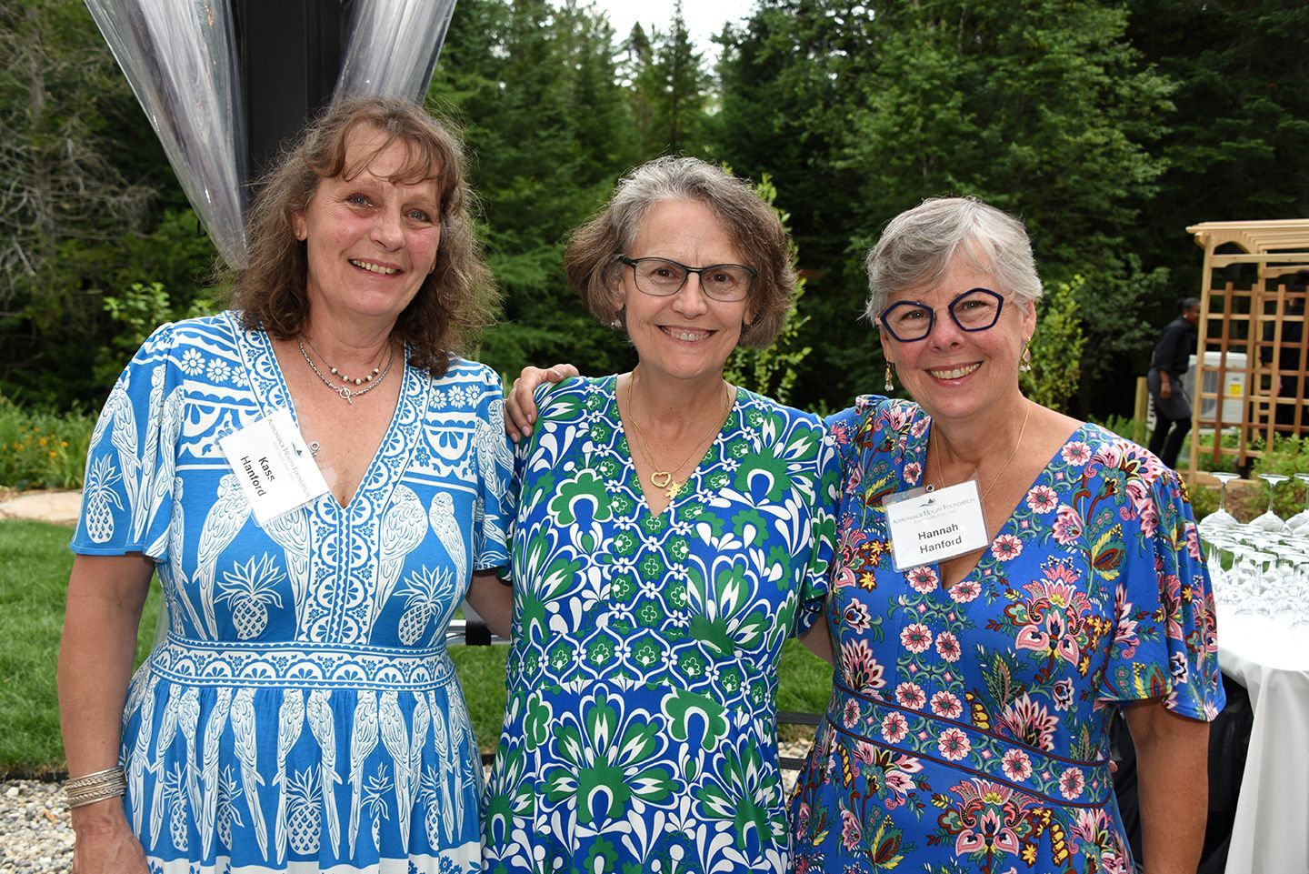 Three women in summer dresses, smiling and posed with arms around each other outside.