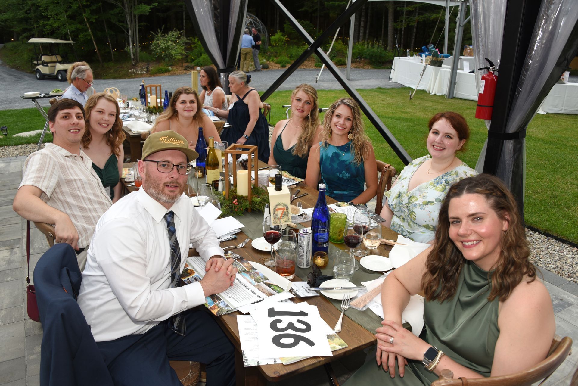 A group of people seated around a table at an outdoor event. They are smiling and appear to be enjoying themselves.