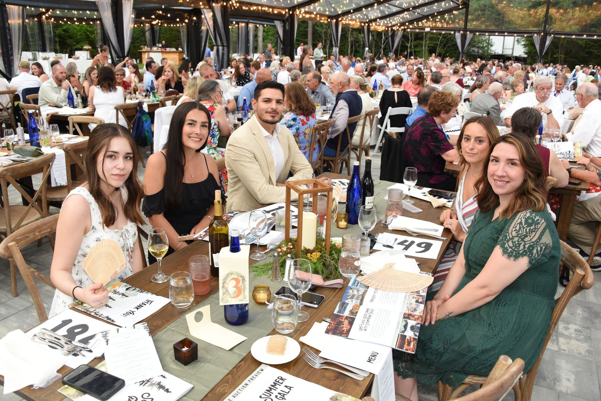 A group of people at a formal outdoor dinner party, seated around a decorated table.