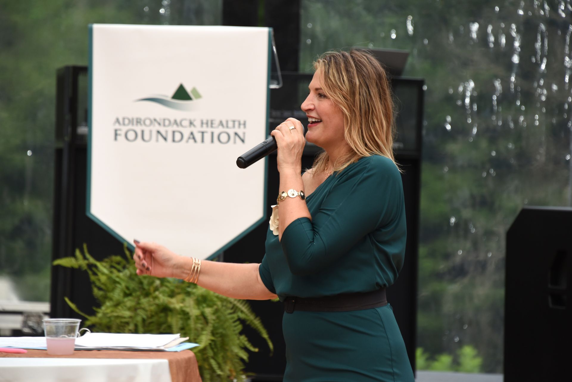 Woman speaking into a microphone at an Adirondack Health Foundation event, wearing a green dress.