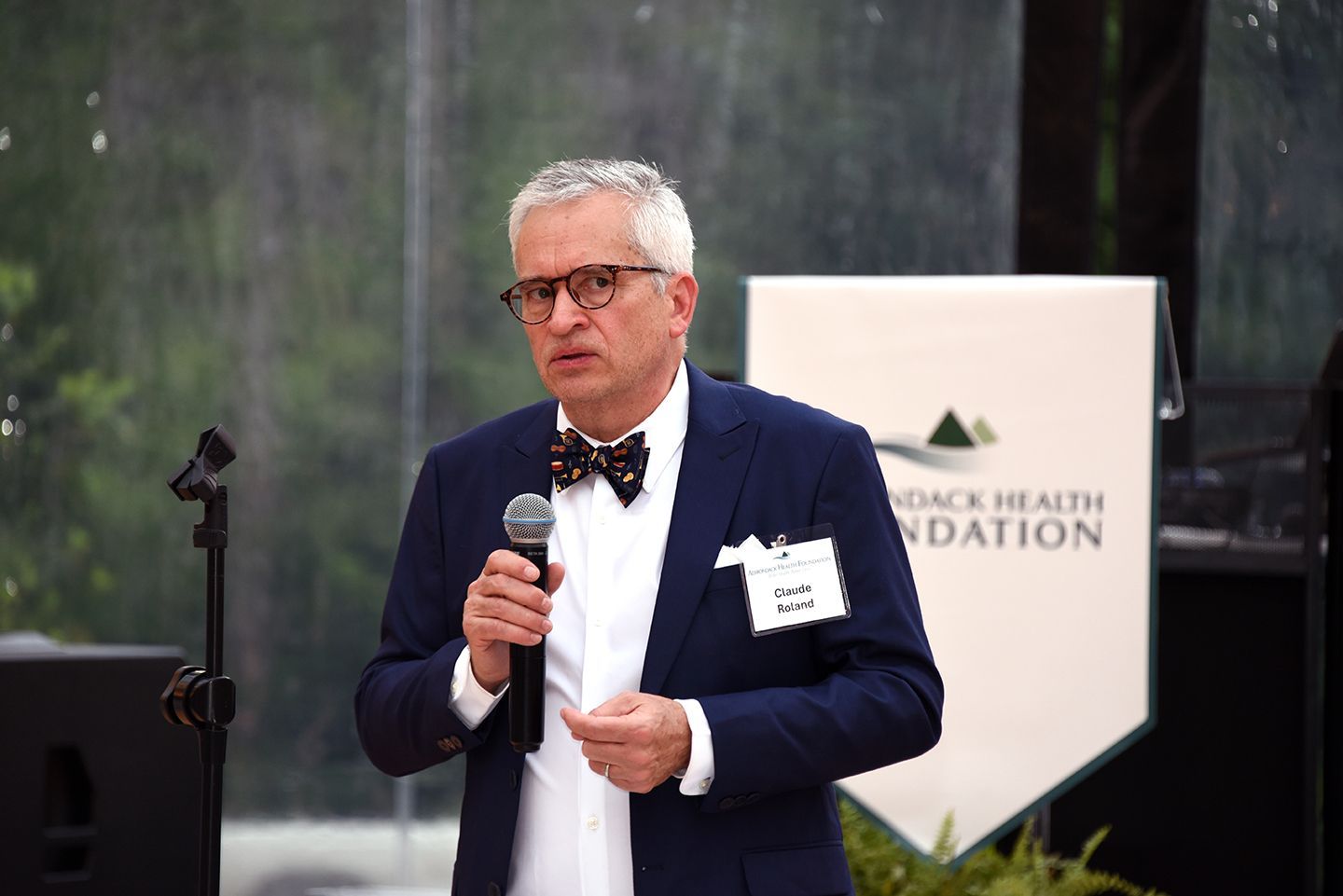 Man in a blue blazer and bow tie speaking into a microphone at a podium with 