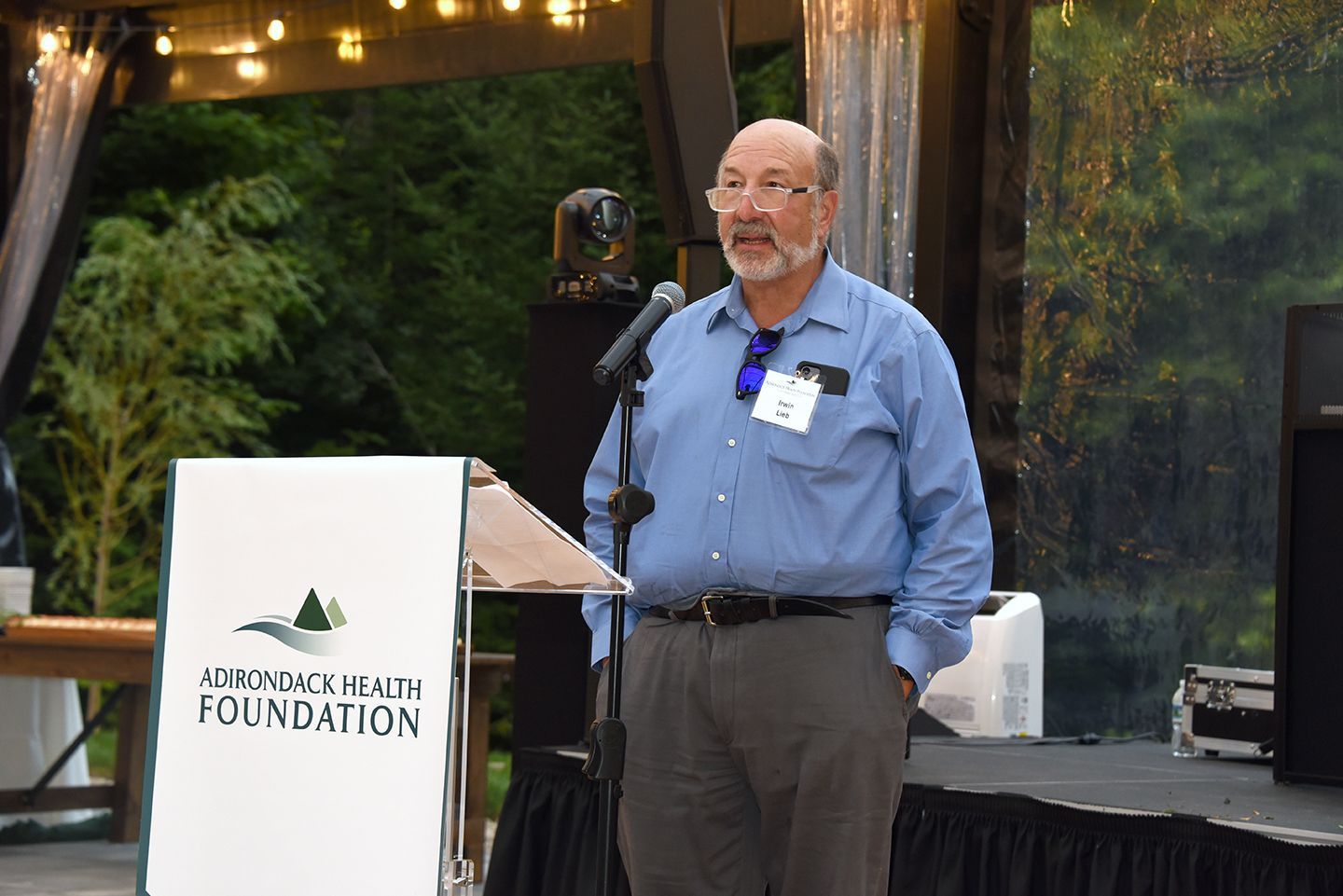 A man with a beard gives a speech at a podium with the 