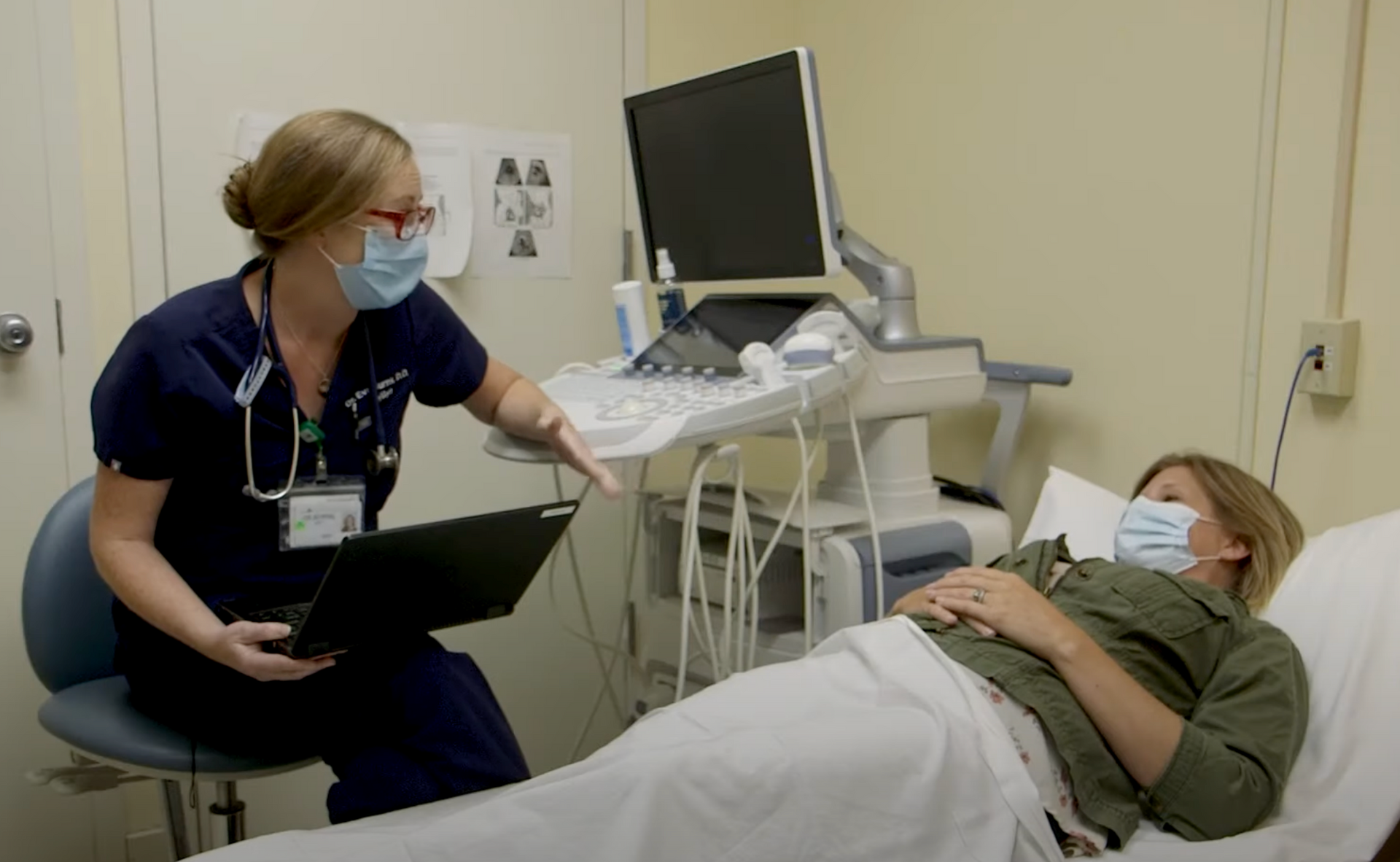 A medical professional wearing a mask explains to a patient wearing a mask.