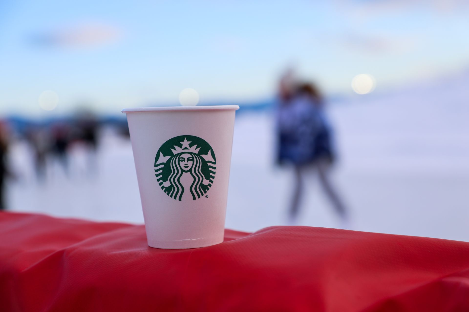 Starbucks coffee cup on a red surface, with blurred skaters and a snowy backdrop.