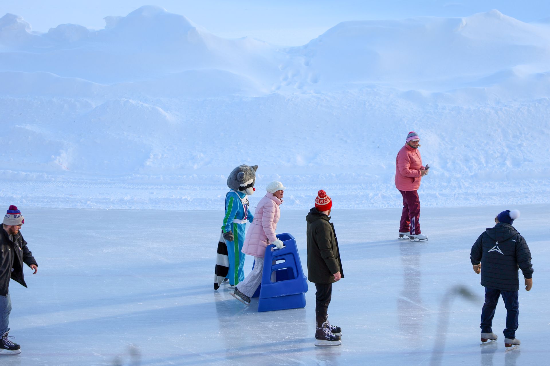 People ice skating on a frozen lake with snowy landscape backdrop.