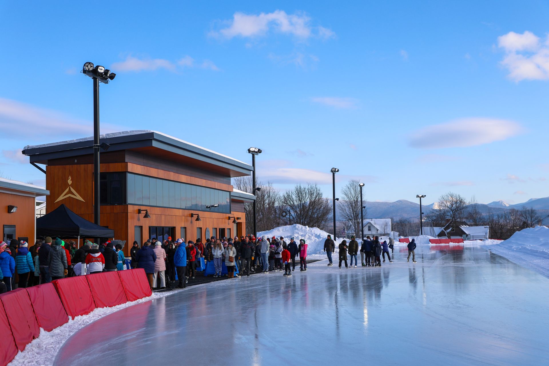 Outdoor ice skating rink with people gathered near a wooden building.