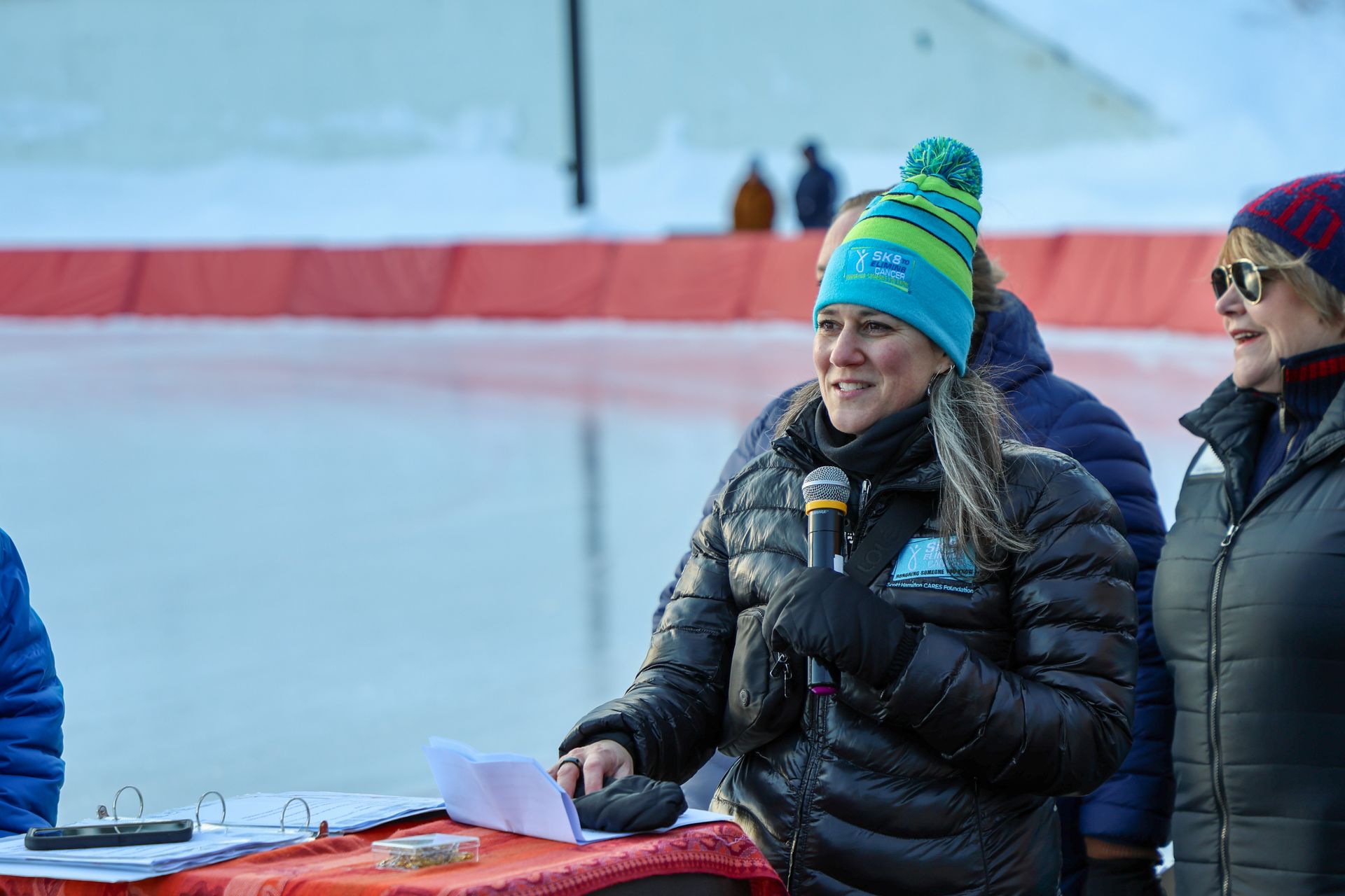 Woman in winter gear speaks into a microphone at an outdoor event. 