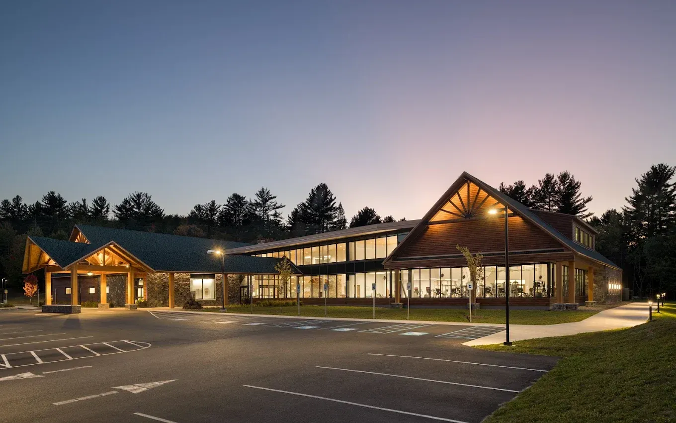 Exterior of a modern lodge-style building at dusk, with warm lighting illuminating the entrance and windows.