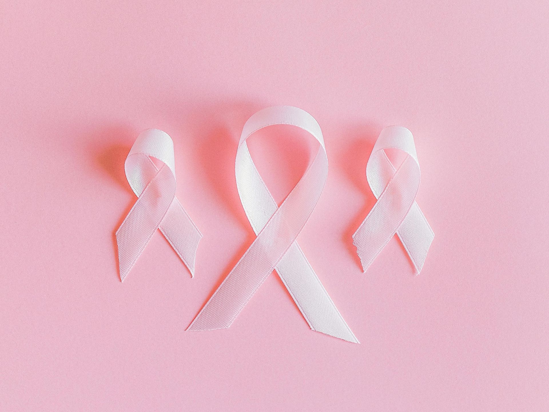 Three pink ribbons, symbols of breast cancer awareness, on a light pink background.