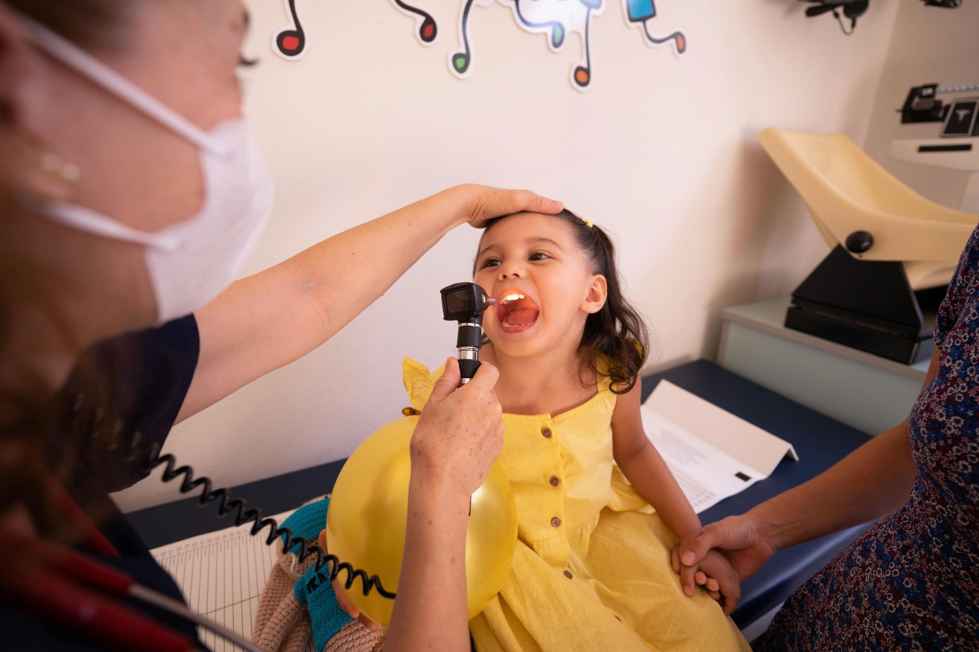 Doctor examining a young girl's throat with a light in a medical office.