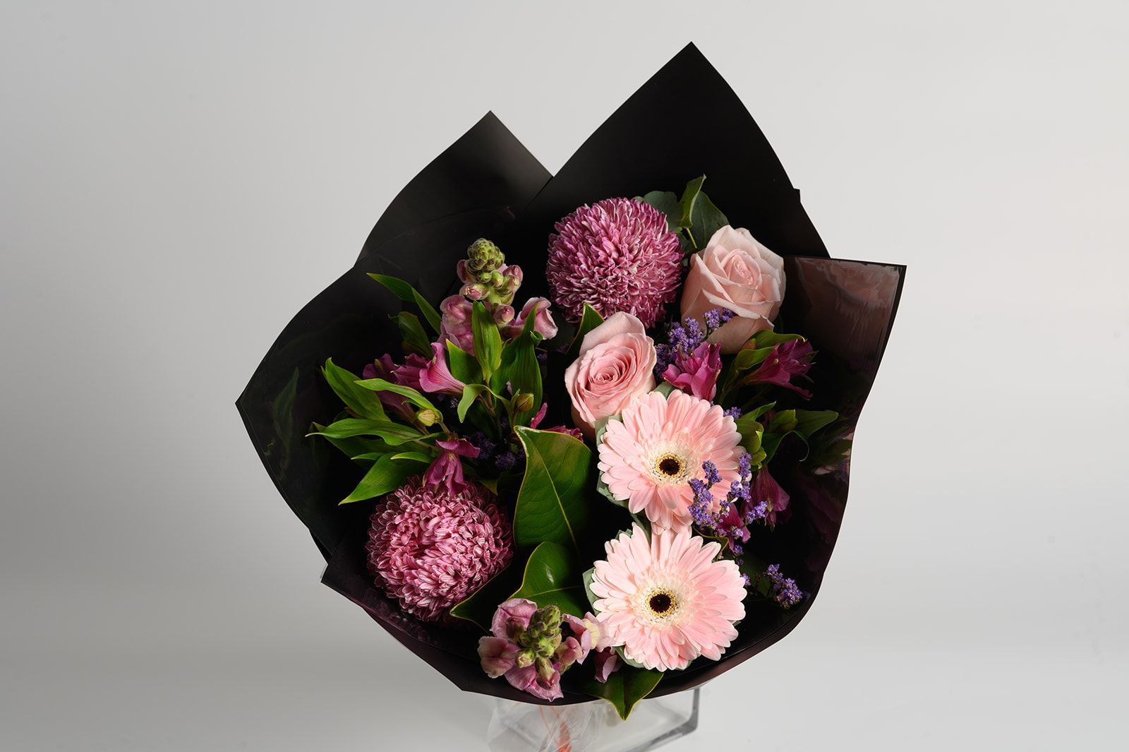 Bouquet of pink and purple flowers wrapped in black paper.
