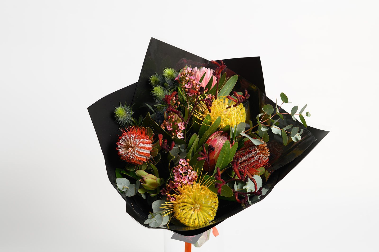 Bouquet of colorful flowers wrapped in black paper against a white backdrop.