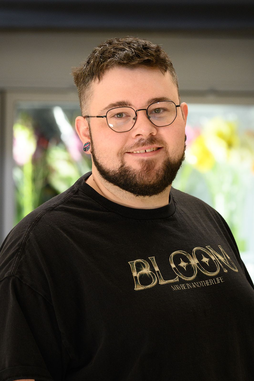 Man with glasses and beard wearing a black t-shirt smiles indoors.