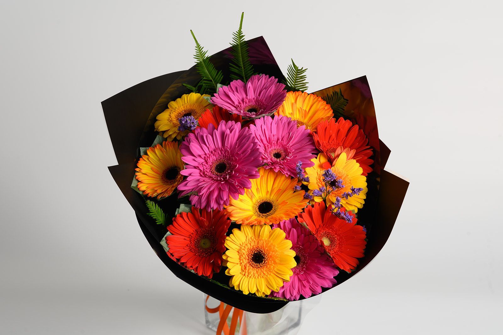 Bouquet of colorful gerbera daisies in shades of pink, orange, and yellow wrapped in black paper.