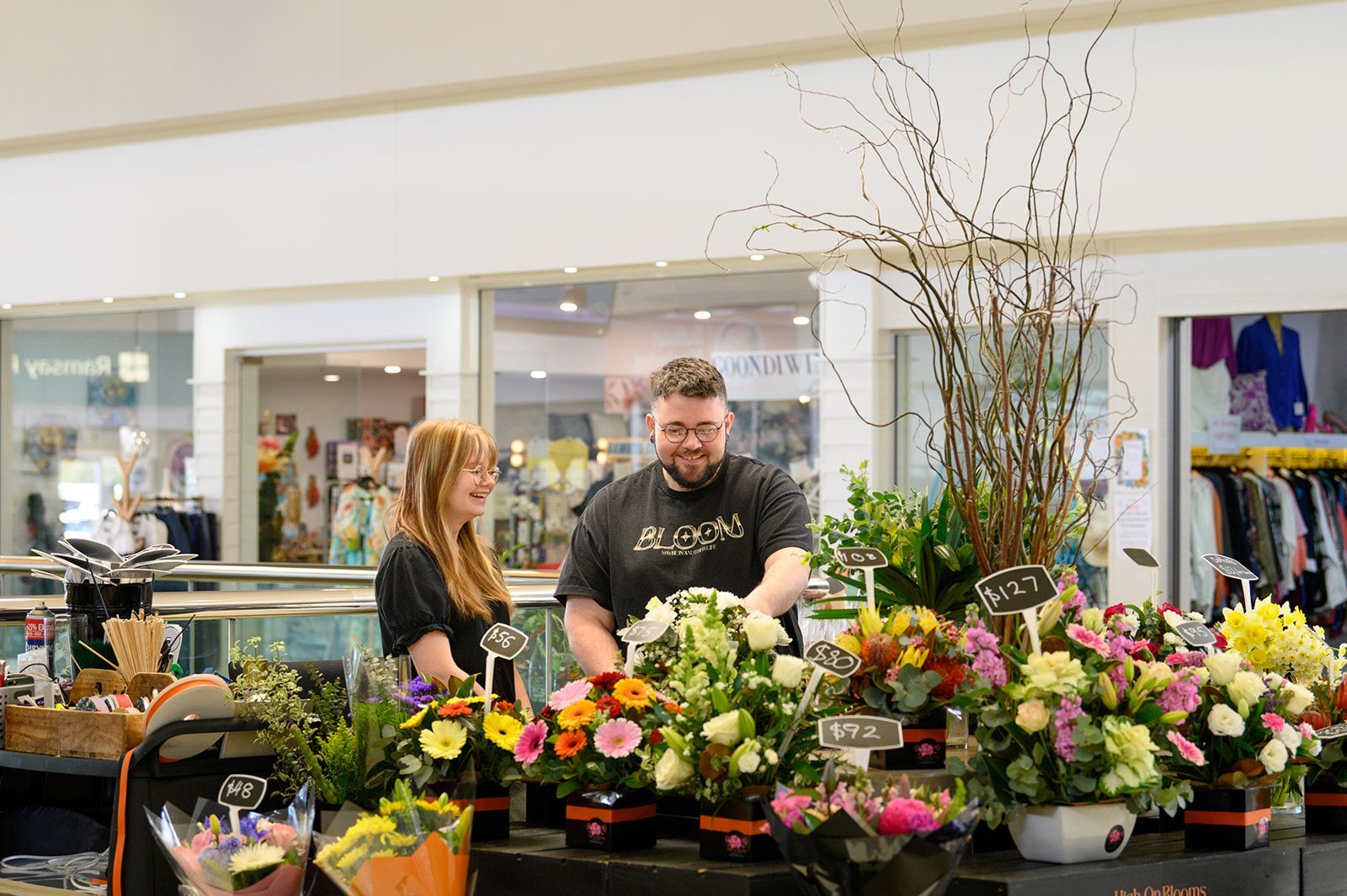 Two people arranging flowers at a floral shop counter, colorful blooms displayed.