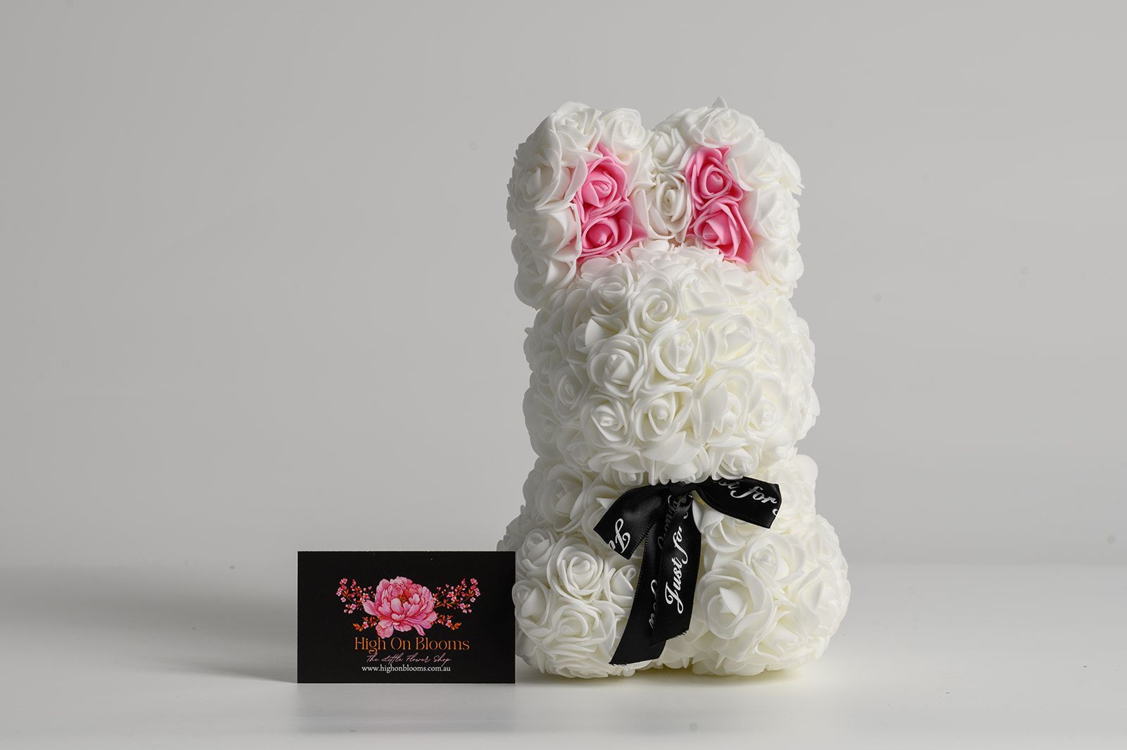 White rose bunny sculpture with pink ear details and black ribbon bow, next to a business card.