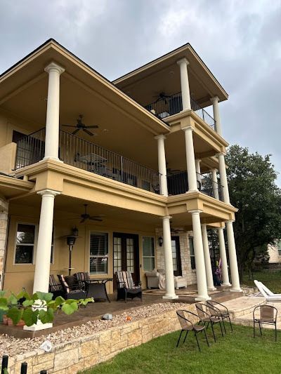 Multi-story house with columns and balconies. Yellow exterior, green lawn, cloudy sky.