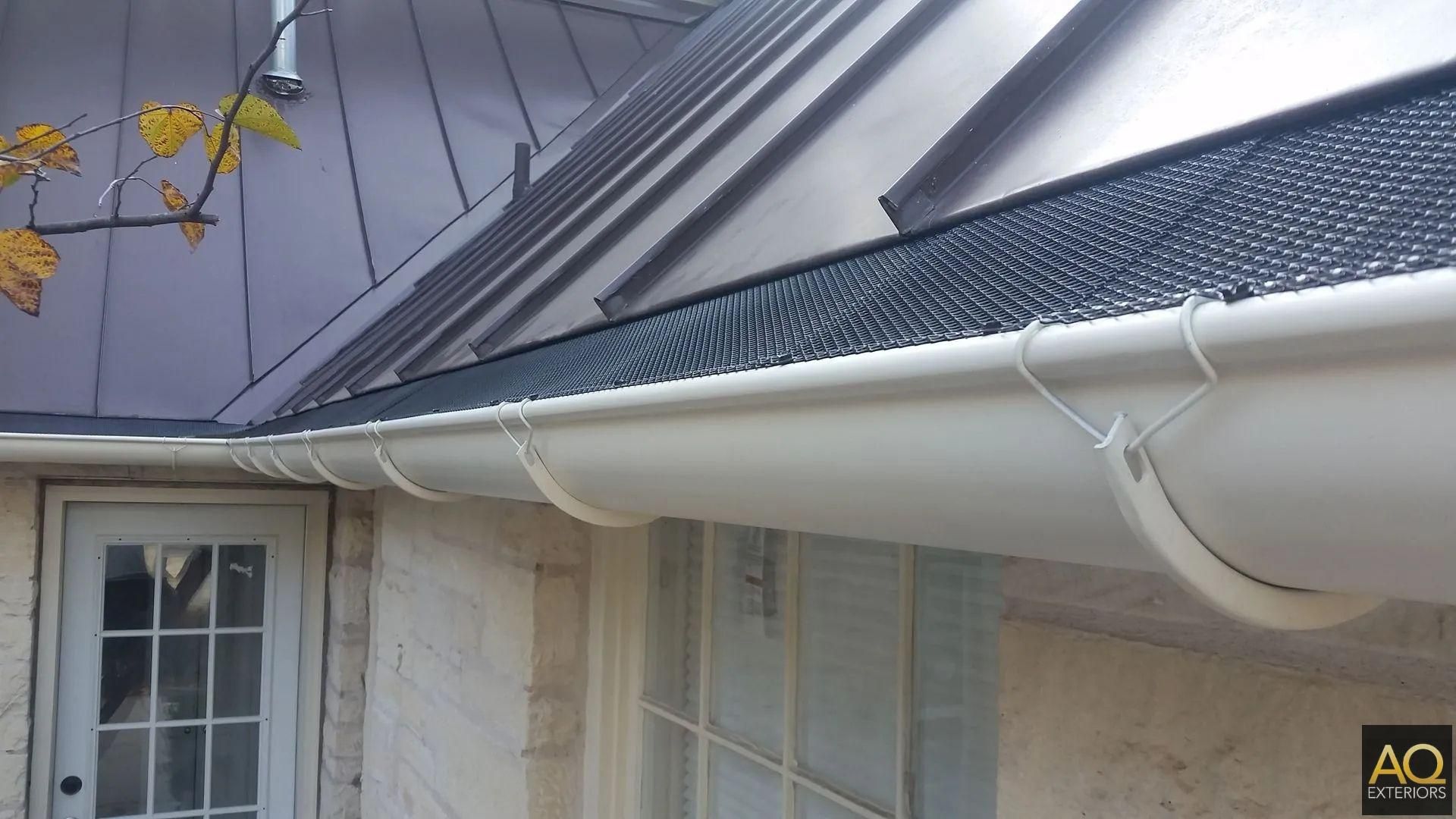White gutters along a house with a dark metal roof. A gutter guard is visible.