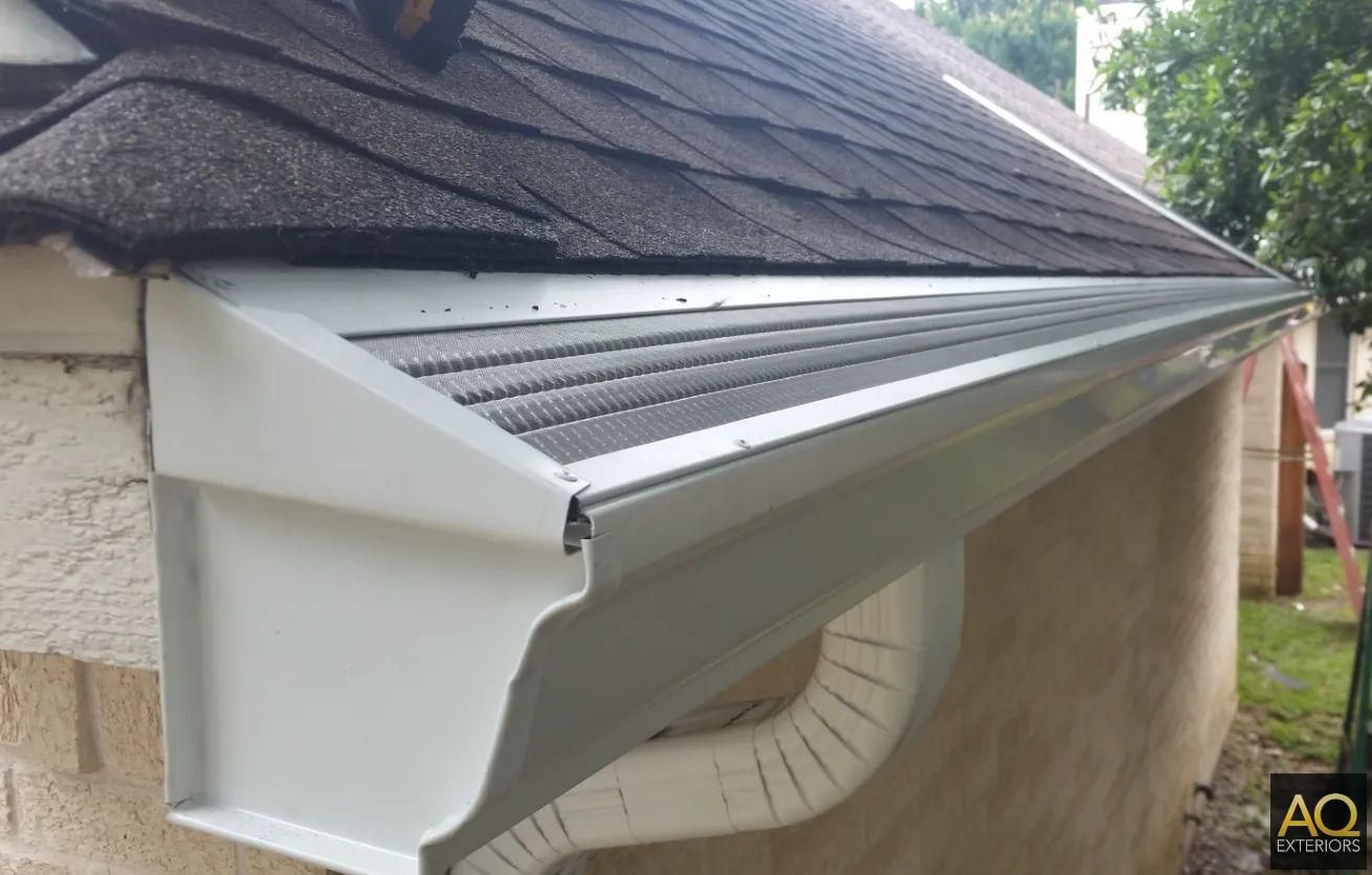 White gutters along a dark shingled roof, over a light-colored brick building.