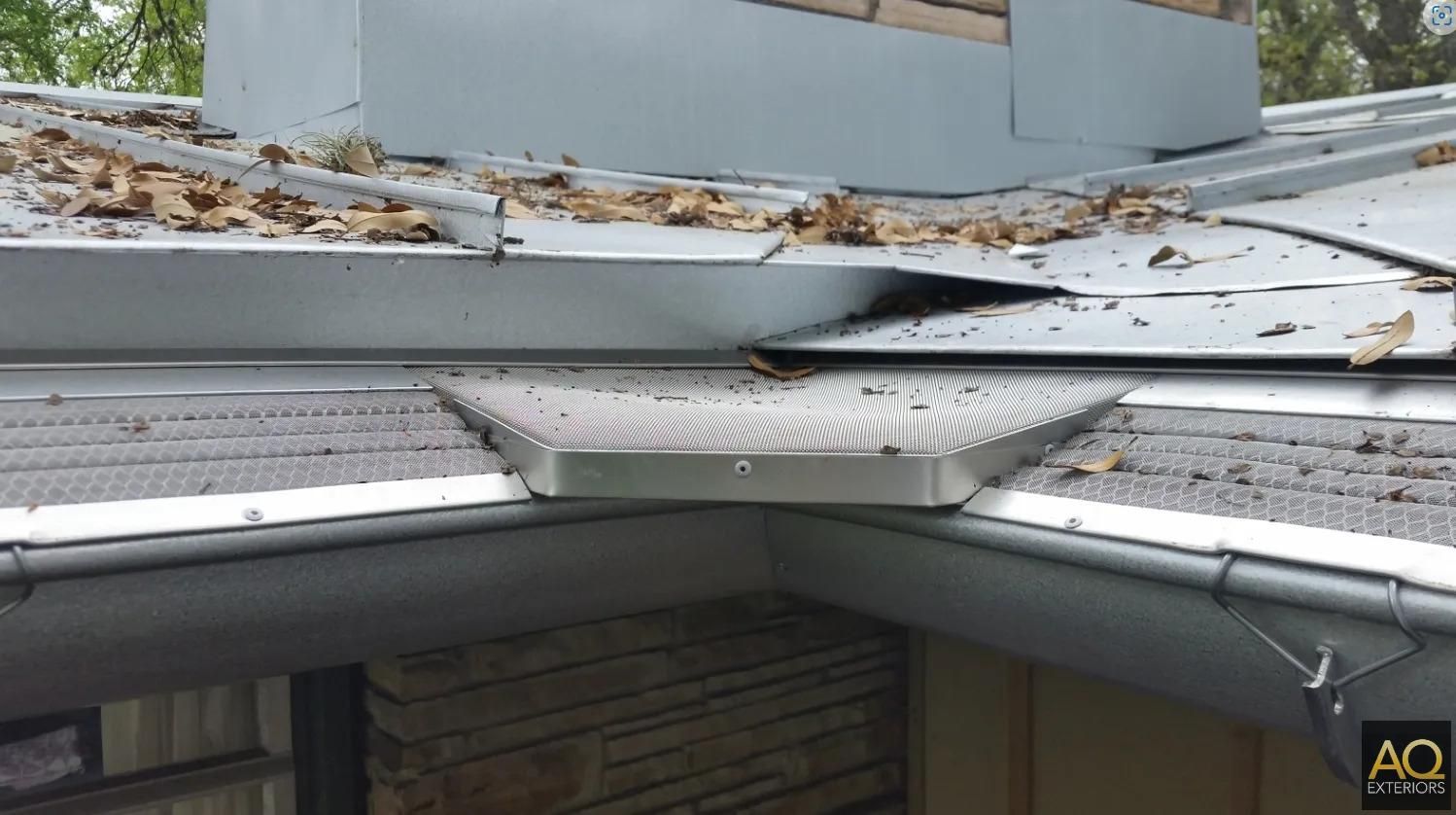A metal roof covered in leaves, with a gutter system and a small chimney in the background.