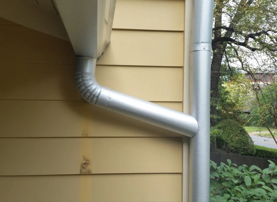 Galvanized metal rain gutter and downspout on a white house with patterned siding.