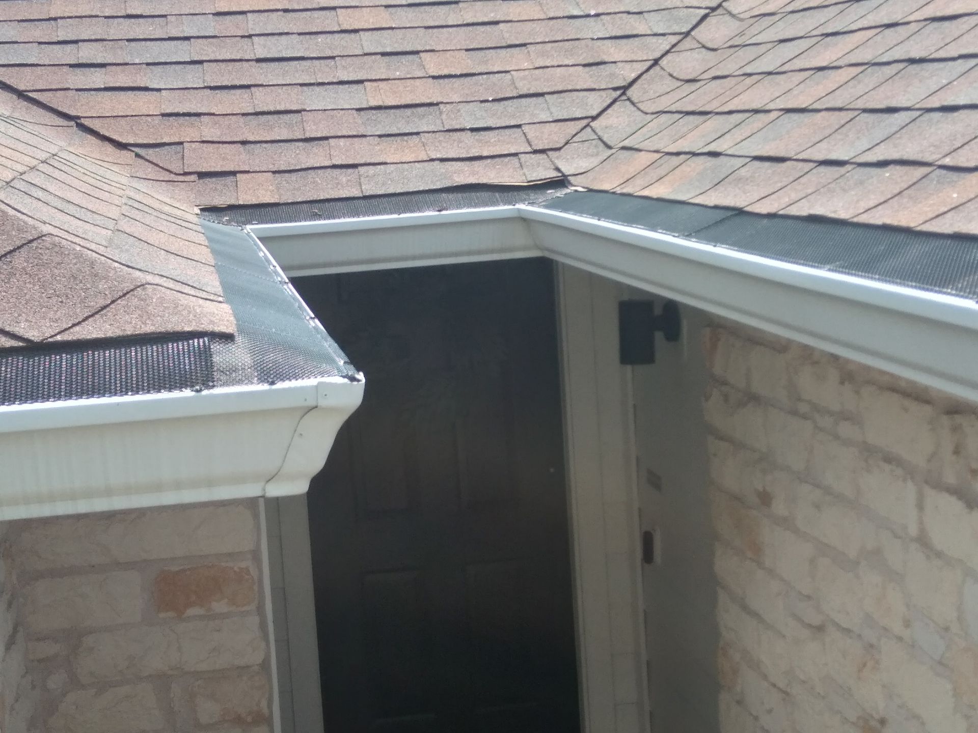 Brown shingle roof with white gutters and brick and stone wall.
