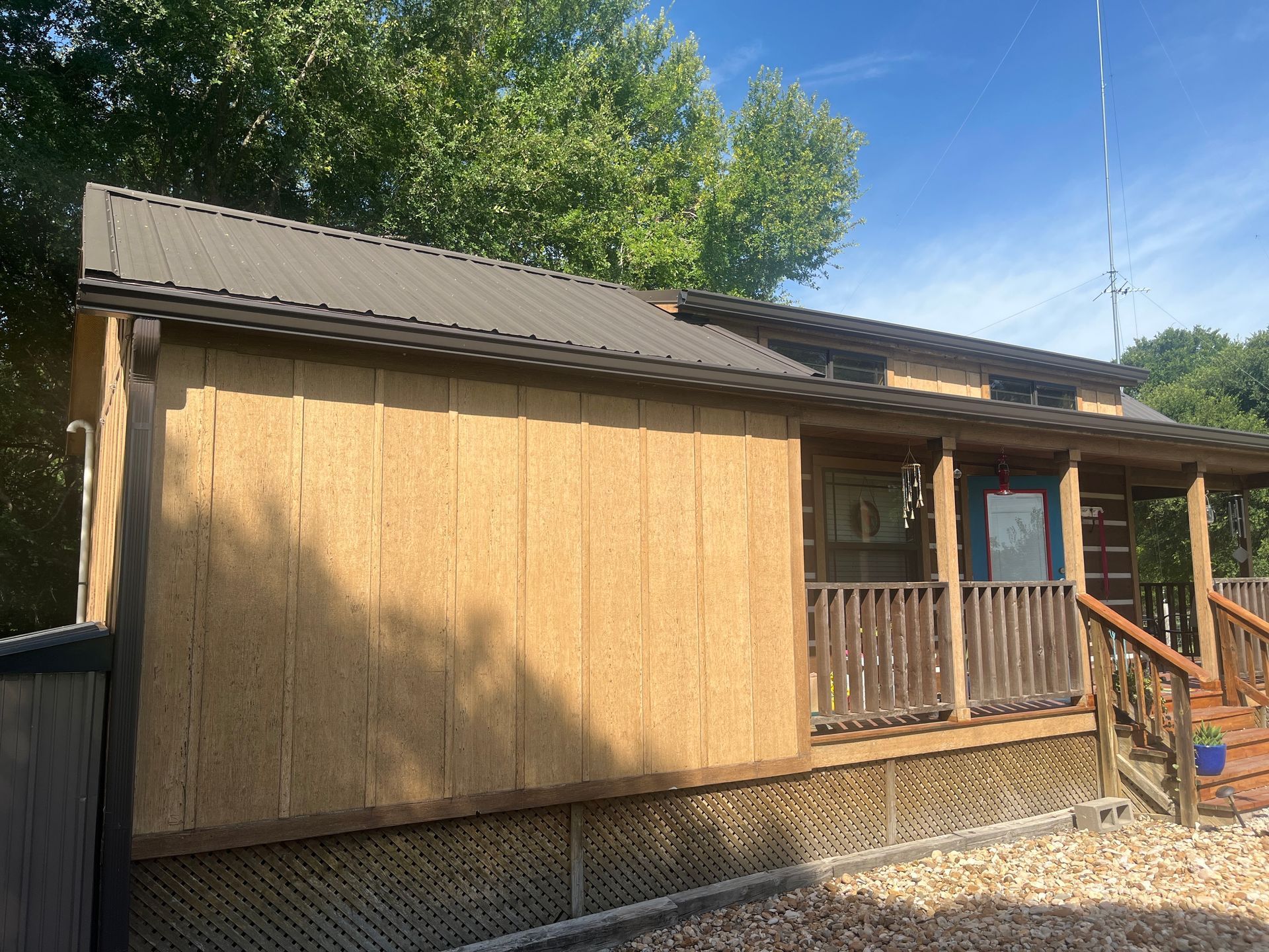 Tan cabin with metal roof, wooden porch, and steps on a sunny day.