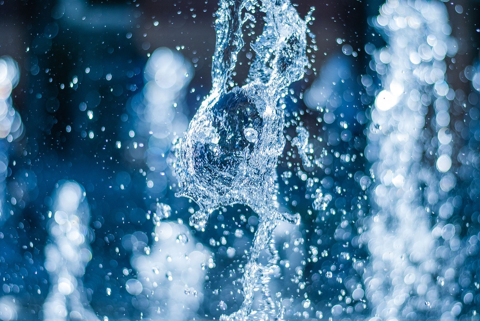 A close-up, high-speed capture of water splashing and droplets spraying against a blurred, deep-blue background.