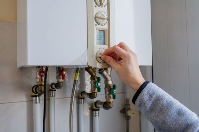 A technician in safety gear uses a wrench to adjust a wall-mounted heating system manifold with copper and white pipes.