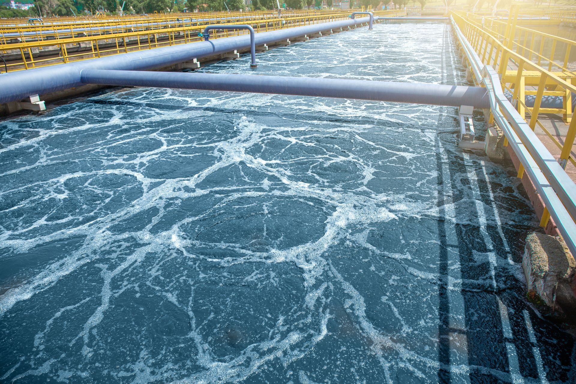 An aeration tank in a wastewater treatment plant with bubbly, agitated water and industrial pipes.
