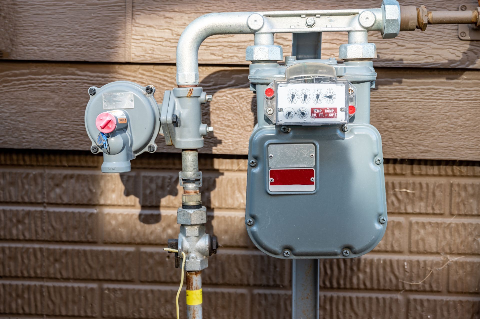 A gray natural gas meter with a regulator valve mounted on a brick exterior wall.