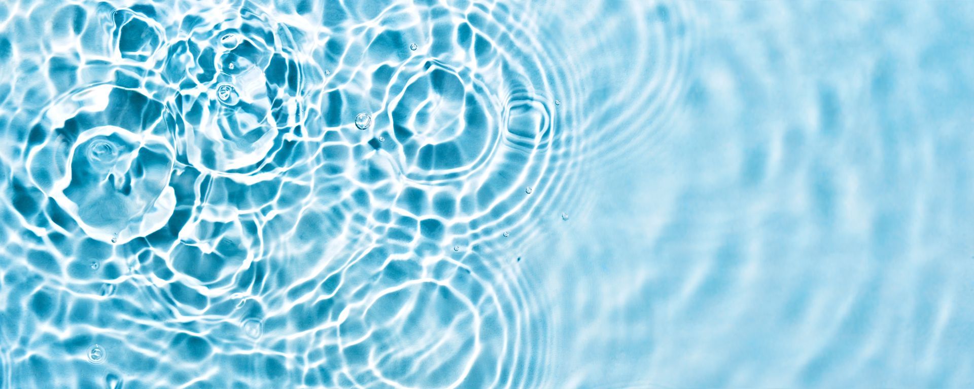 Close-up of light blue water surface with ripple patterns caused by falling droplets.