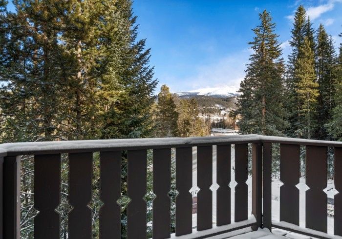 A balcony with a wooden railing overlooking a forest and mountains.