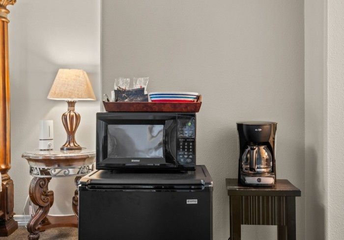 A microwave is sitting on top of a small refrigerator next to a coffee maker.