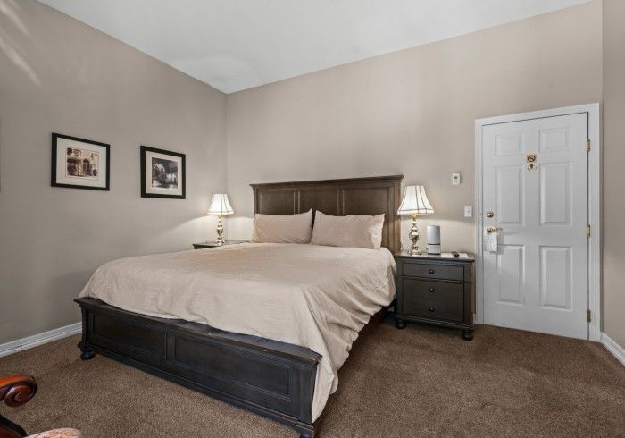 A bedroom with a king size bed , nightstand , lamps and a door.