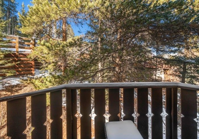 A wooden deck with a chair on it and trees in the background.